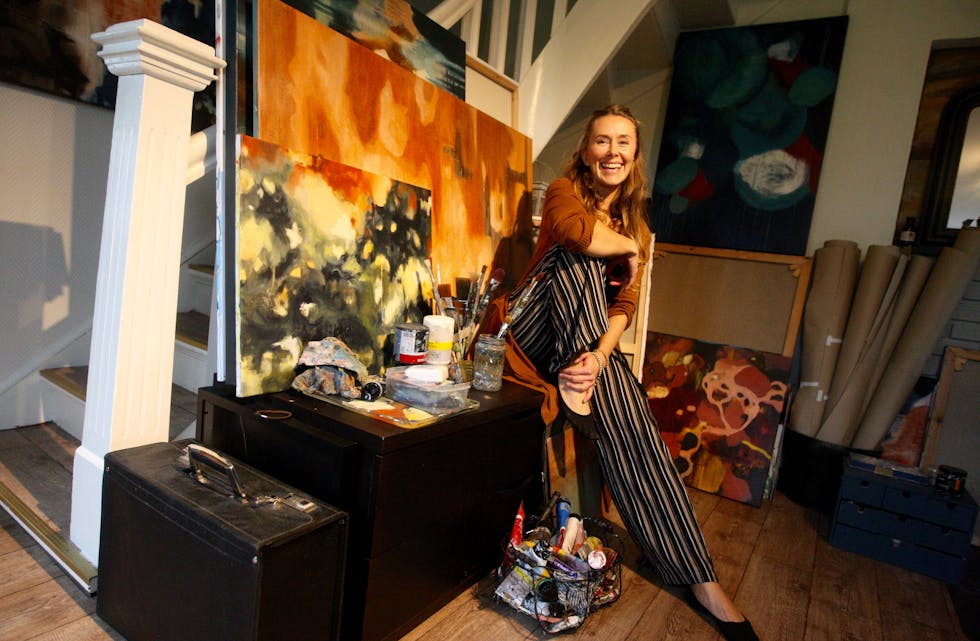 Linda Renate Andersen i stova som også fungerer som arbeidsrom. Dei flotte bileta er stort sett måla i jordnære fargar, noko heile stova hennar ber preg av.
Foto: Alf-Einar Kvalavåg