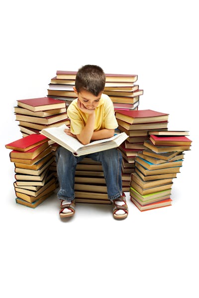 Photo of young boy reading a book while sitting on books